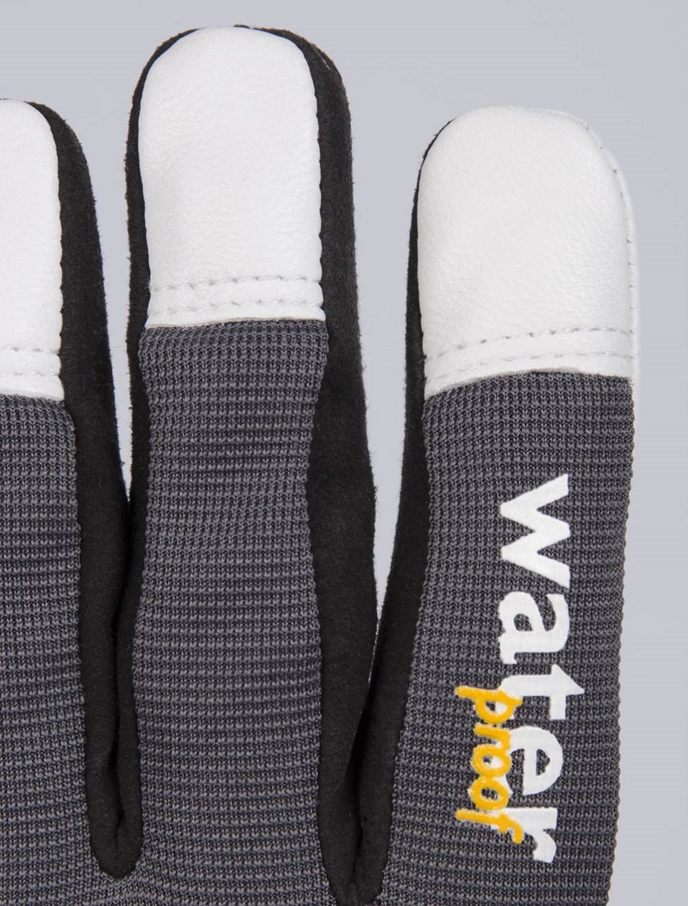 Nahaufnahme eines dunkelgrauen Handschuhs mit drei Fingern. Weiße, glatte Fingerkuppen, Rest aus fein strukturiertem dunklem Gewebe. Auf dem Zeigefinger steht vertikal „Water“ und darunter gelb „Proof“. Hellgrauer Hintergrund.