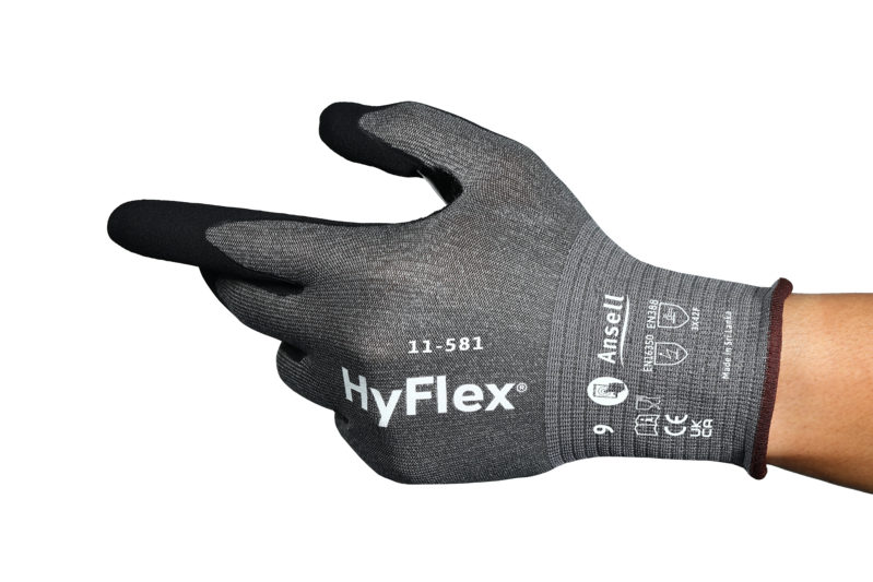 Une main porte un gant anti-coupures HyFlex 11-581 gris Ansell, avec bouts de doigts noirs compatibles écrans tactiles. Le dos montre le logo HyFlex, le modèle et les symboles EN388. Orienté à gauche.